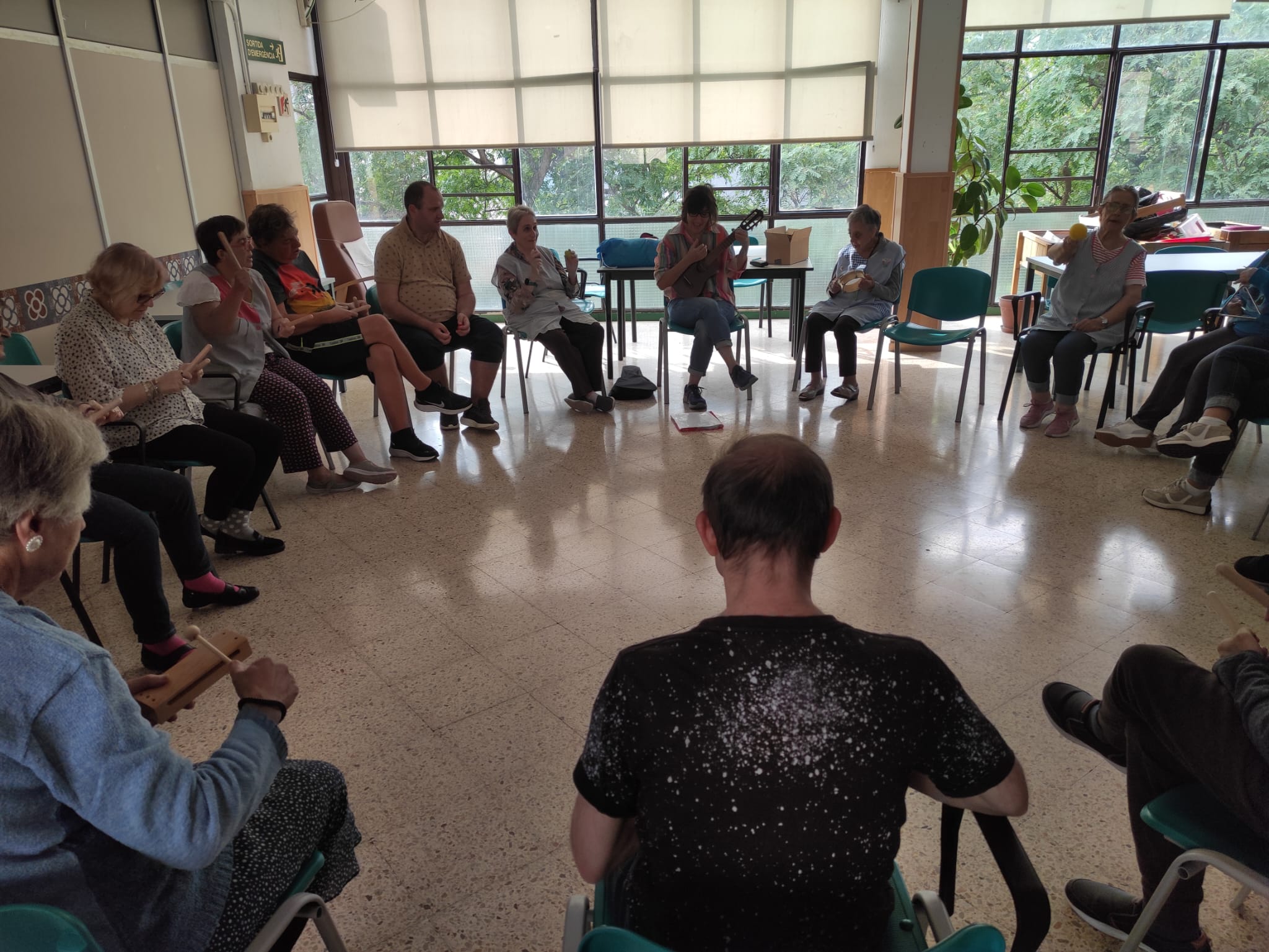 Taller de Musicoterapia con los usuarios sentados en círculo tocando un instrumento con la profesora tocando el ukelele.