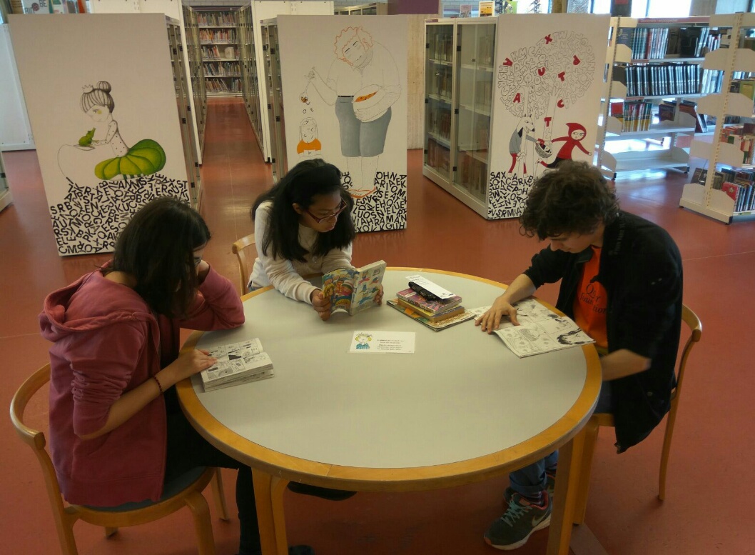 Fotografia de 3 usuaris en una taula de la biblioteca llegint llibres.
